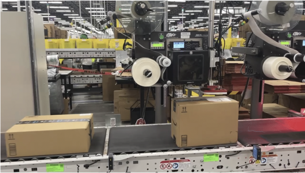Photo from an Amazon fulfillment center showing boxes on a conveyor belt getting prepped for delivery.
